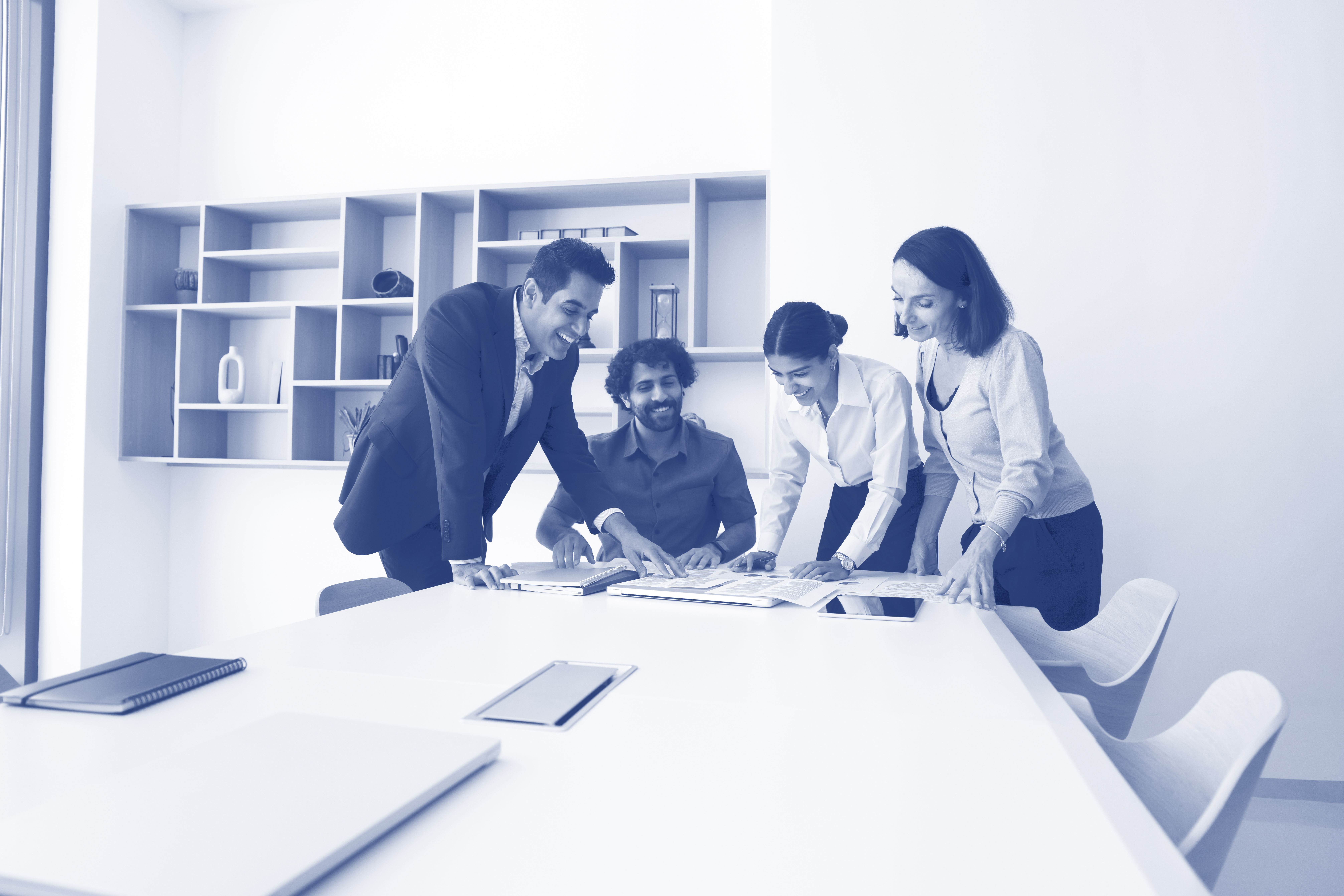 Four multicultural colleagues gather together for paperwork around conference table