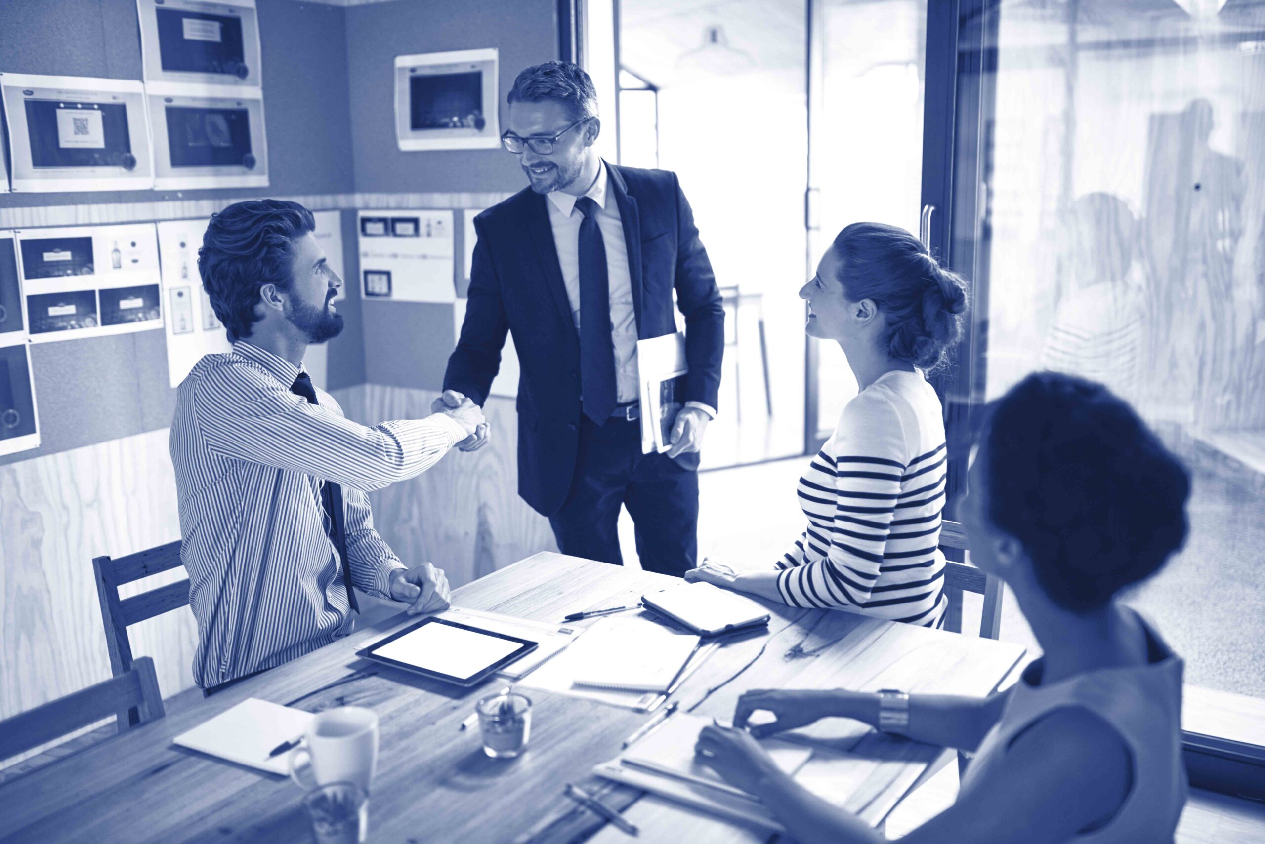 Hell bring a new energy to the team. Shot of two businesspeople shaking hands in an office while colleagues look on.